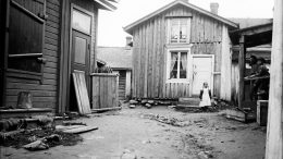 Tyttö seisoo Nuotanperän poikkikadulla Iin kirkonkylässä. Kuva on vuodelta 1913. Kuva: Samuli Paulaharju, Museovirasto.