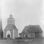 Haukiputaan kirkko ja kellotapuli vuonna1896 näyttivät tältä. Rakennuksissa oli alkuun tummempi maalipinta. Kuvan on ottanut Armas Lindgren. Kirkko ja kellotapuli valmistuivat vuonna 1762. Kirkkopihalla ei kasvanut tuolloin puita tai pensaita.