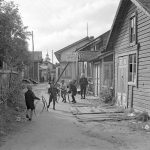 Pikkupojat vanteita pyörittämässä Kahvila Sointulan (O. Helmivirta) edustalla vuonna 1935. Taustalla Iin vanhan kirkon kellotapuli ja oikealla Helmivirran leipomo, kauppa ja kahvila Sointula. Kirkko tuhoutui tulipalossa 1942. Kuva: Pietinen, Museovirasto.