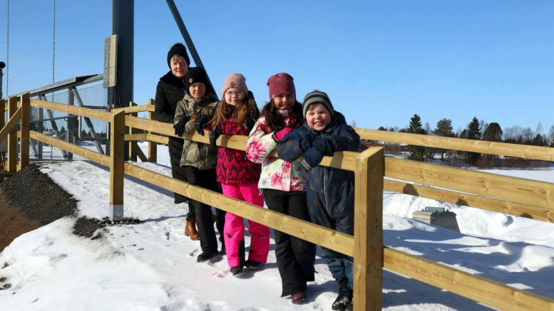 Jakun koulun oppilaat (oikealta) Tiitus, Mileah, Hilda ja Daniel sekä koulunjohtaja Anu ovat kulkeneet siltaa pitkin jo useamman kuukauden ajan, eikä joen ylittäminen tunnu pelottavalta. Lapset tietävät, miten sillalla käyttäydytään; sillalla ei saa pyöräillä, juosta tai pomppia ja kaiteille kiipeily on myös kielletty. (Kuva: Iin kunta)