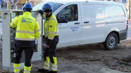 Mittarien vaihtajat liikkuvat Iin Energian logolla varustetulla autolla sekä käyttävät myös logolla varustettuja työasuja. Iin keskustaajamassa mittarikaapin äärellä Jussi Kärsämä (selin) ja Harri Tölli.