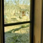 Osa harmaan talon ikkunoista on lasitettu vanhalla puhalletulla ikkunalasilla. Se on vihertävää ja vääristää taustan maiseman.
