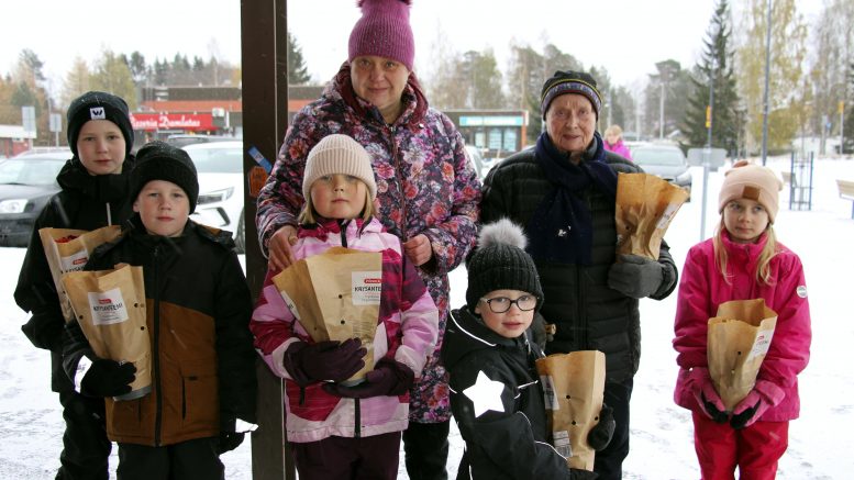 Leena Kokko (vas.) ja lapset Jare, Joan ja June Heikkinen, Nella Pahkala ja Linnea Sorvali olivat jakamassa krysanteemeja Haukiputaan torilla sunnuntaina. Kukkasen sai myös asemakyläläinen Anni Huru, joka oli ilahtunut ikäihmisille suunnatusta tempauksesta. Kuva Auli Haapala