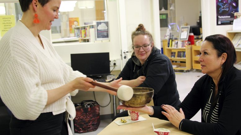 Paula Harju asettaa äänimaljan Jaana Lamminpartaan kämmenelle ja kumauttaa sitä. Vierellä Susanna Honkala, jolle äänimalja antoi erilaiset soinnut.