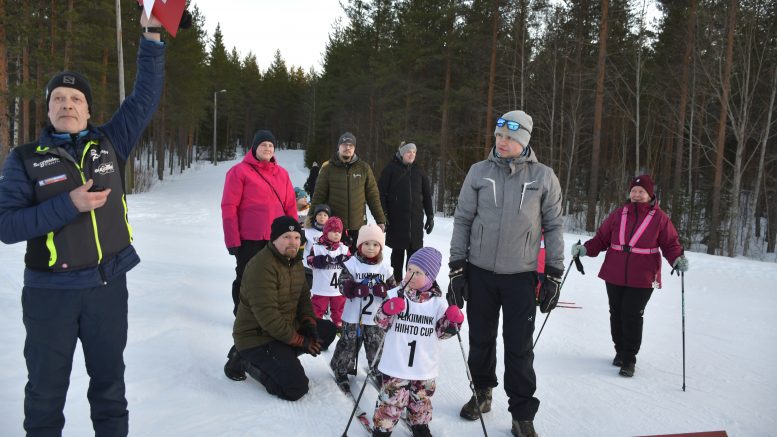 Vuonna 2020 ja myöhemmin syntyneet hiihtäjät huoltajineen ovat valmiina lähtöön Ylikiimingin hiihtocupin vuoden 2024 viimeiseen osakilpailuun. Asko Perätalo (vas.) näyttää maalin ajanottajille merkkiä, että päätöskisan ensimmäinen lähtö on valmiina.