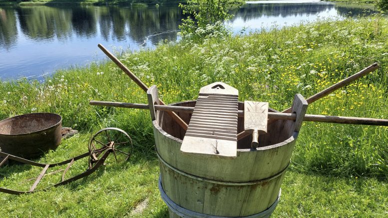 Kuvassa oleva saavi on nähnyt 147 juhannuspyykkäystä. Saavin korvakkeisiin on aseteltu pyykkipulikka kantamisen apuvälineeksi. Pulikan päällä pyykkilauta ja pesukurikka. Muuripata odottaa tulen virittäjää.
