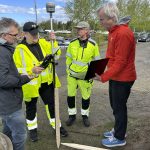 Kellon muotoinen taideteos tarvitsee sille sopivan maaperän ja tukevan perustuksen satama-alueelle. Taiteilija Rasmus Rosengren Nielsenin (oik.) kanssa paikkaa mittomassa Oulun kaupungin työntekijöitä sekä vasemmalla taidetiimin tekninen asiantuntija Sam Collins. Kuva: Claudia Woolgar
