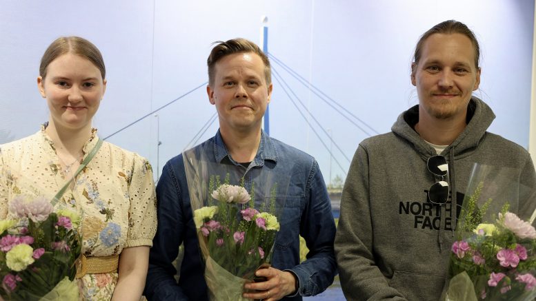 Nämä kylät -kappaleen solisti Emilia Ojala, sanoittaja ja säveltäjä Lasse Rasinkangas ja musiikkivideon tekijä Timo Vehkaoja kukitettiin ja kahvitettiin viime viikolla kunnanvirastolla. Kuva: Aada Alapuranen.