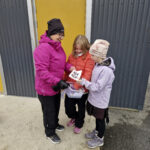 Opettaja Mari Perätalo jakamassa Mila Pirille ja Iiris Keskimäiselle Halloween-radan lappuja.