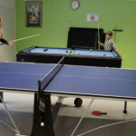 Saini ja Leo mittelivät taitojaan pingispöydän ääressä. Hyvinvointikoordinaattori Marika Erkkilä (takana) pääsi testaamaan pelitaitojaan biljardipöydän ääressä.